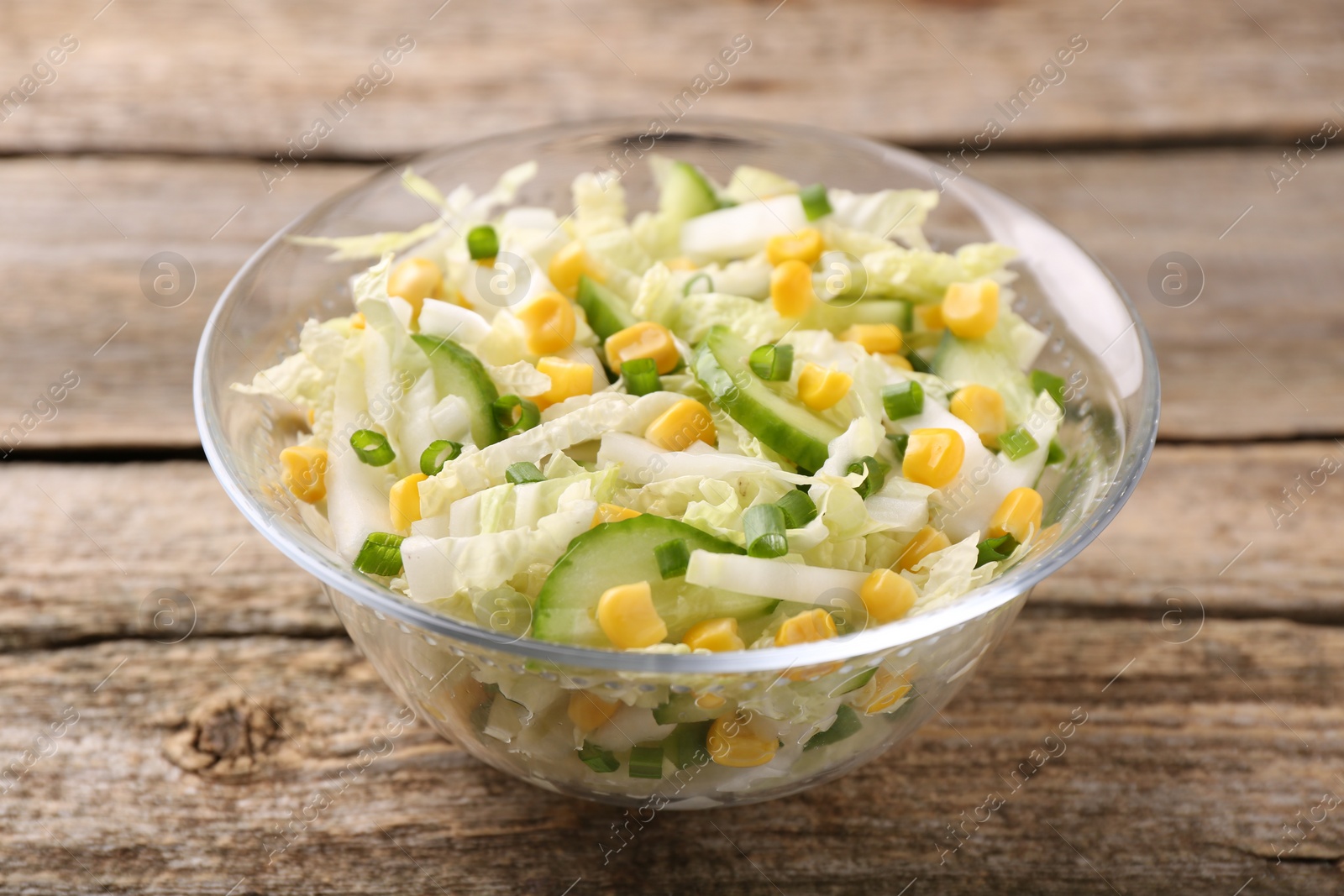 Photo of Tasty salad with Chinese cabbage, corn and cucumber in bowl on wooden table, closeup