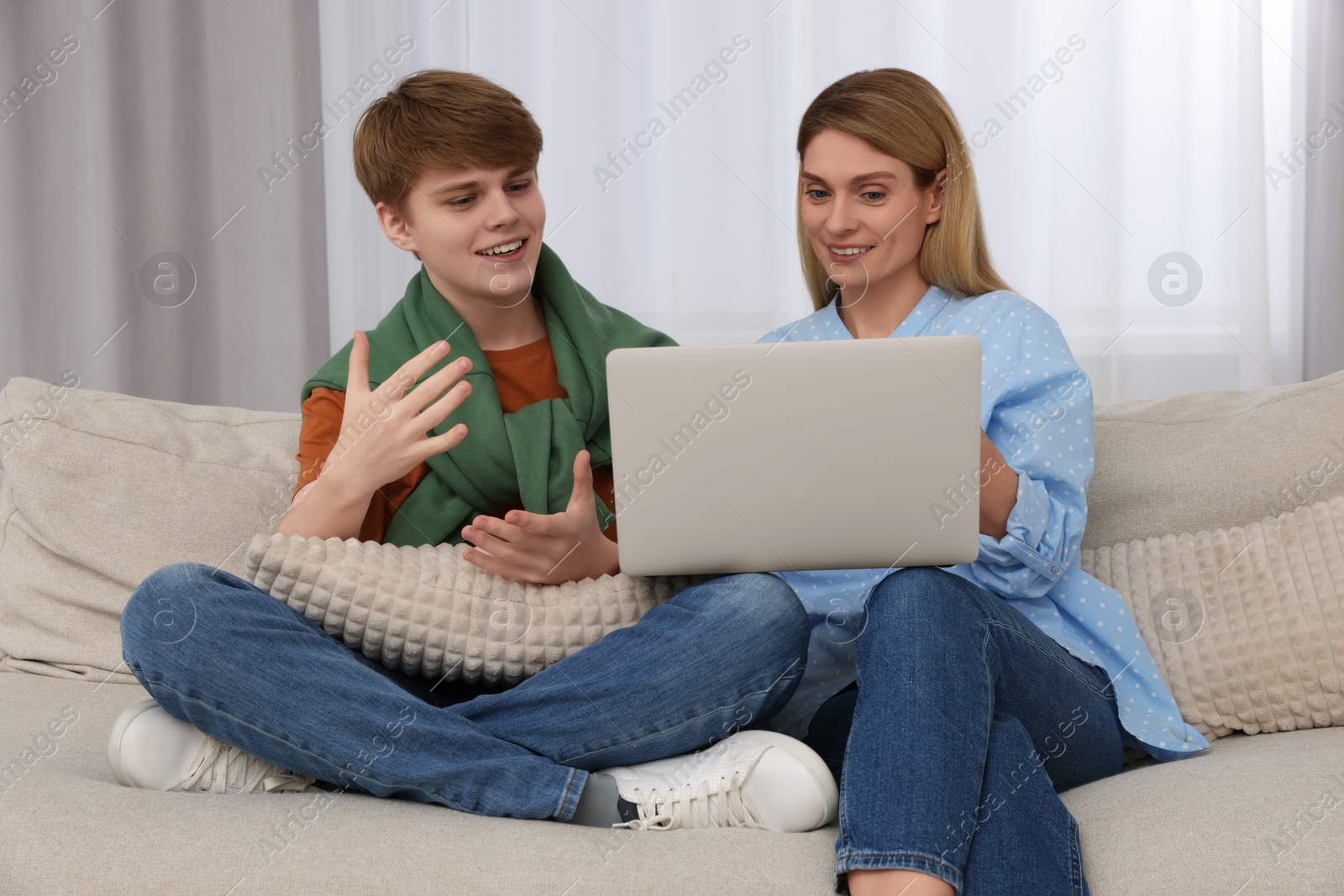 Photo of Happy teenage son and his mother with laptop at home