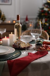 Photo of Christmas table setting with burning candles, appetizers and dishware indoors