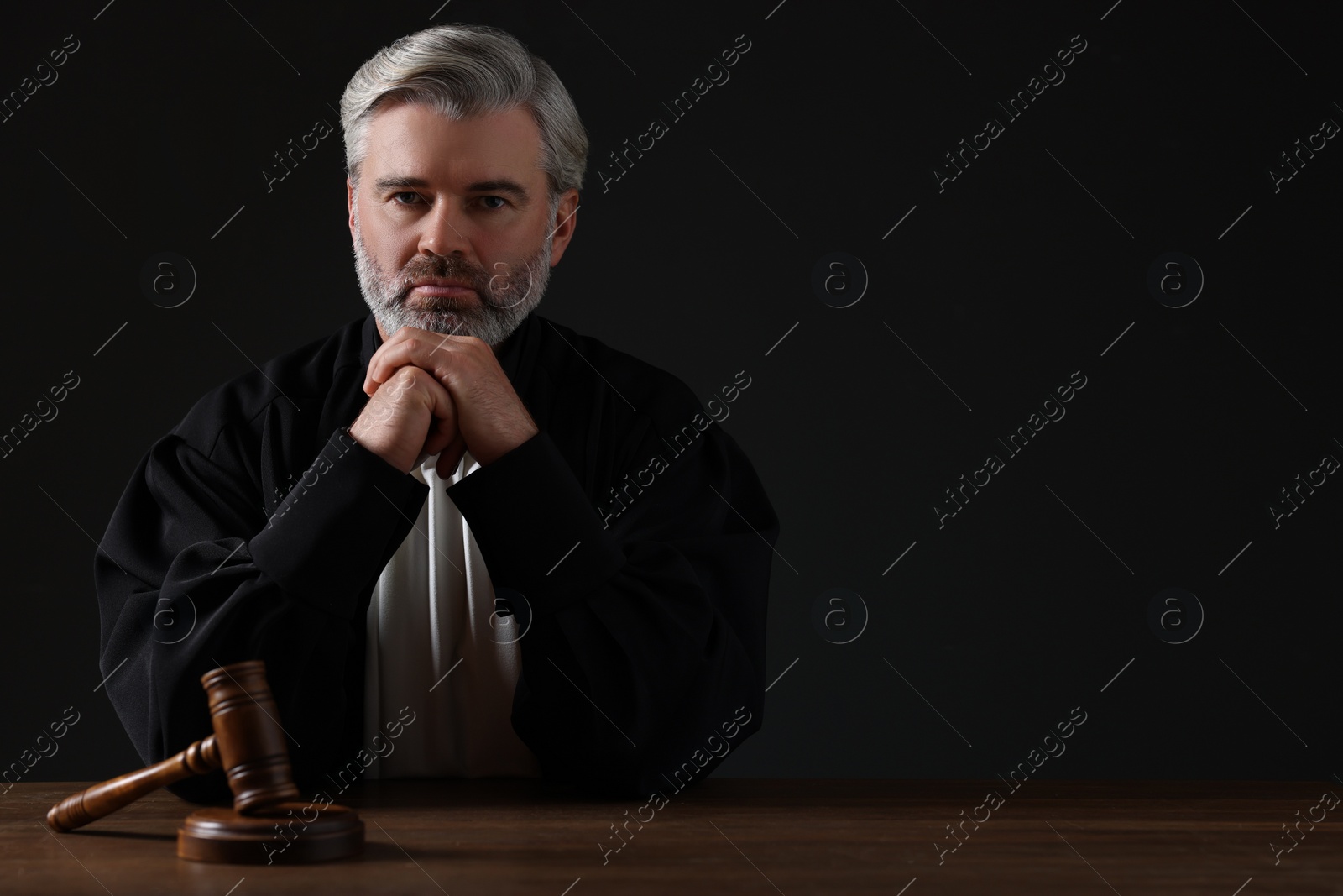 Photo of Judge with gavel sitting at wooden table against black background. Space for text