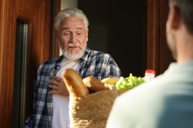 Photo of Man with wicker bag of products helping his senior neighbour outdoors