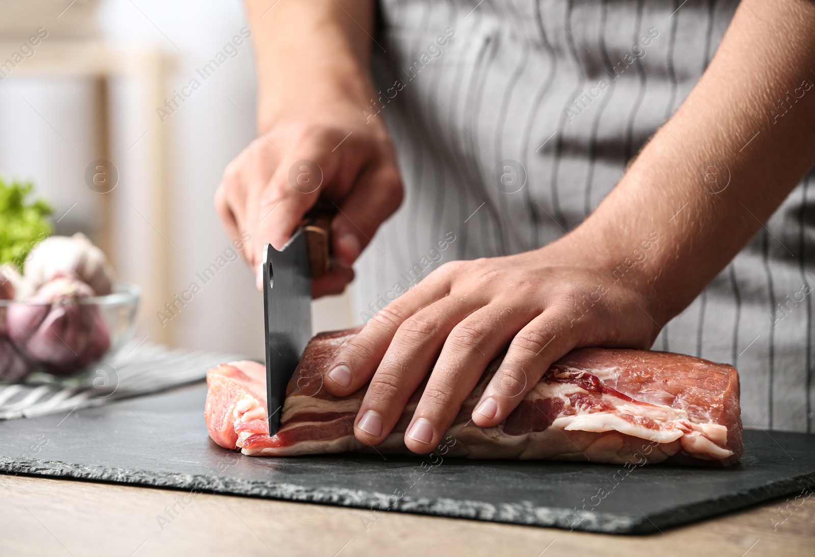 Photo of Man cutting fresh raw meat on table in kitchen, closeup