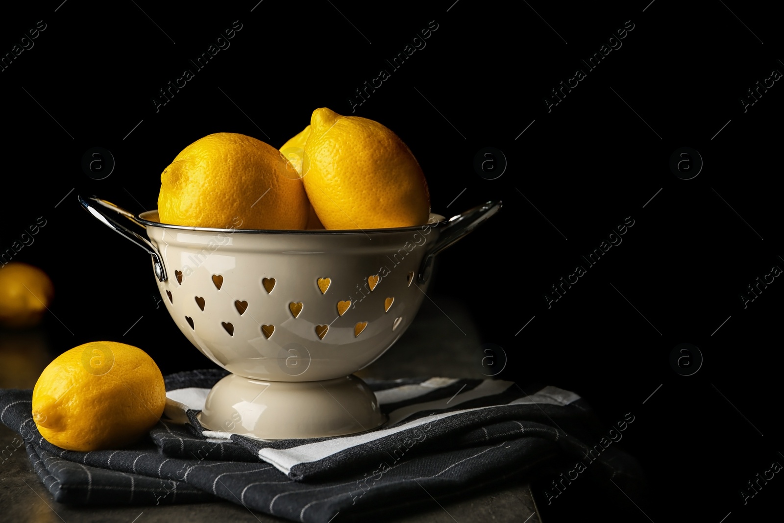 Photo of Colander with whole lemons on table against dark background