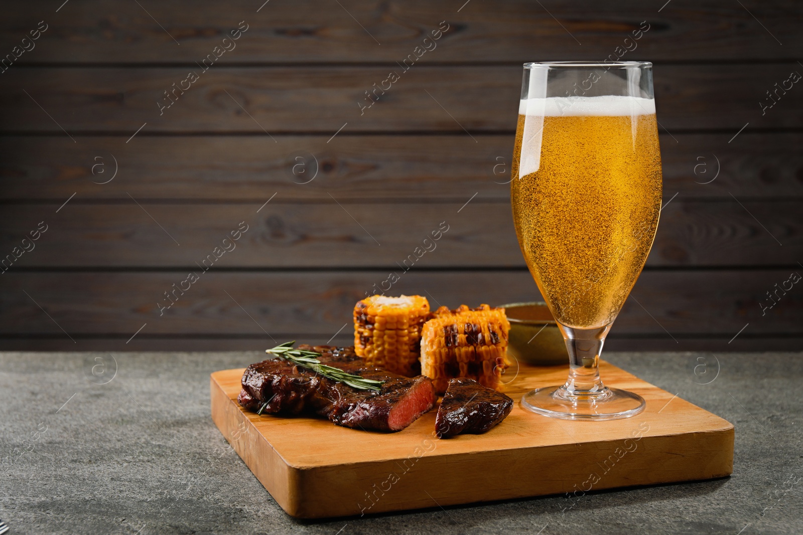 Photo of Glass of beer, delicious fried steak and corn on grey table. Space for text