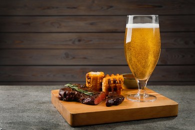 Glass of beer, delicious fried steak and corn on grey table. Space for text