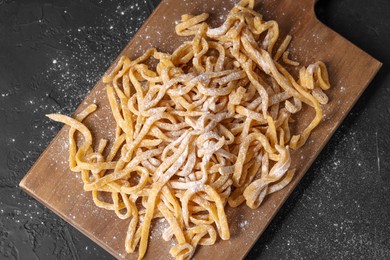 Board with homemade pasta and flour on dark textured table, top view