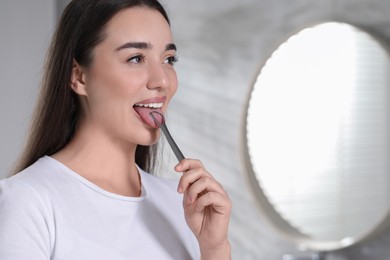 Photo of Happy woman brushing her tongue with cleaner in bathroom, space for text