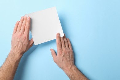 Photo of Man holding sheet of paper on light blue background, top view. Mockup for design