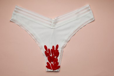 Photo of Woman's panties with red flower petals on peach  background, top view
