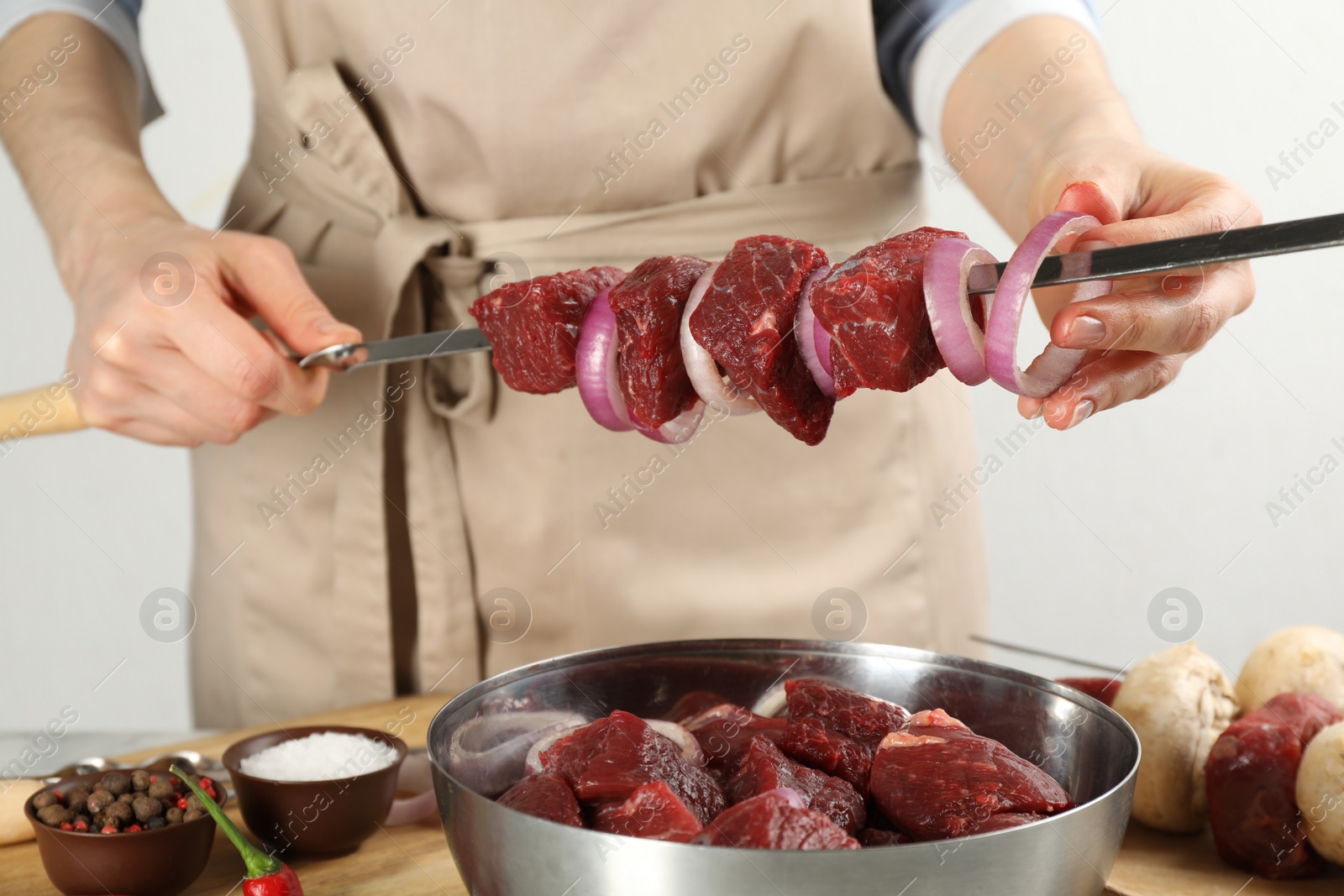 Photo of Woman stringing marinated meat and onion on skewer at table, closeup