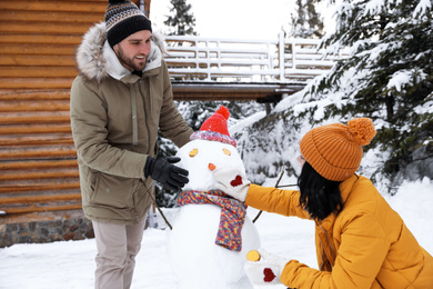 Photo of Happy couple making snowman outdoors. Winter vacation