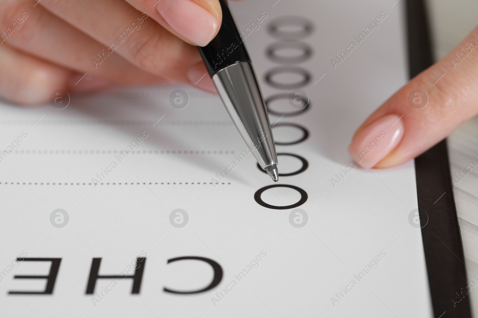 Photo of Woman filling Checklist with pen at table, closeup view