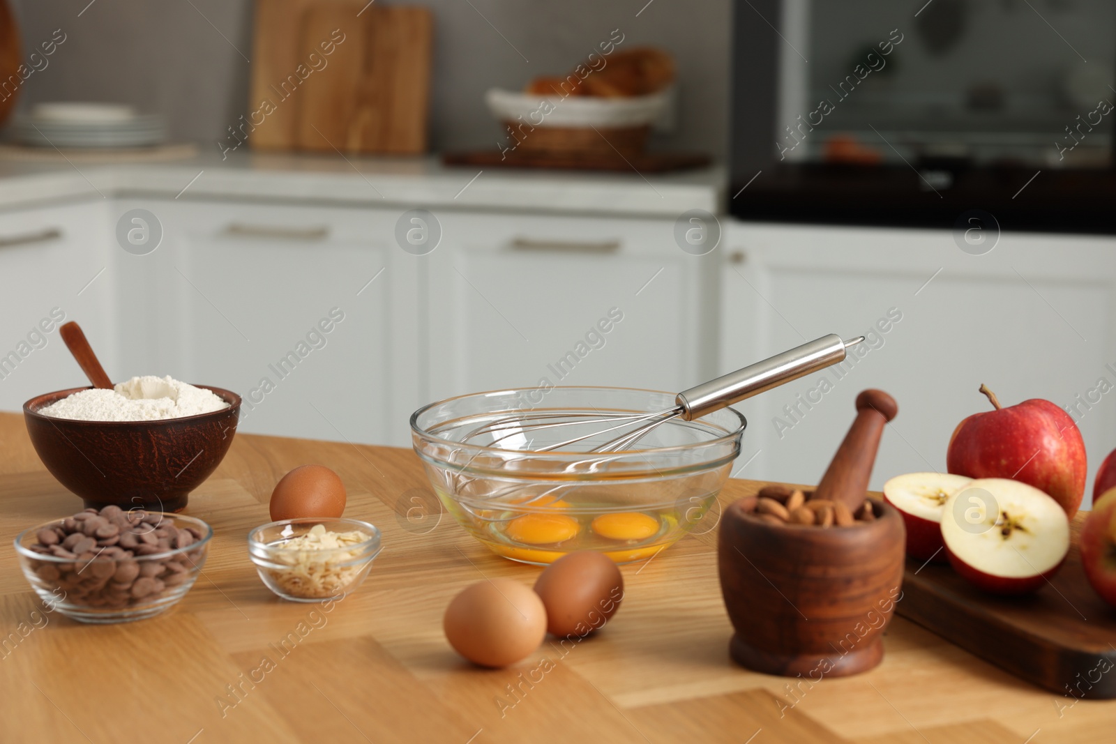 Photo of Cooking process. Metal whisk, bowl and products on wooden table in kitchen