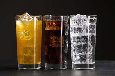 Photo of Glasses of different refreshing soda water with ice cubes on grey table