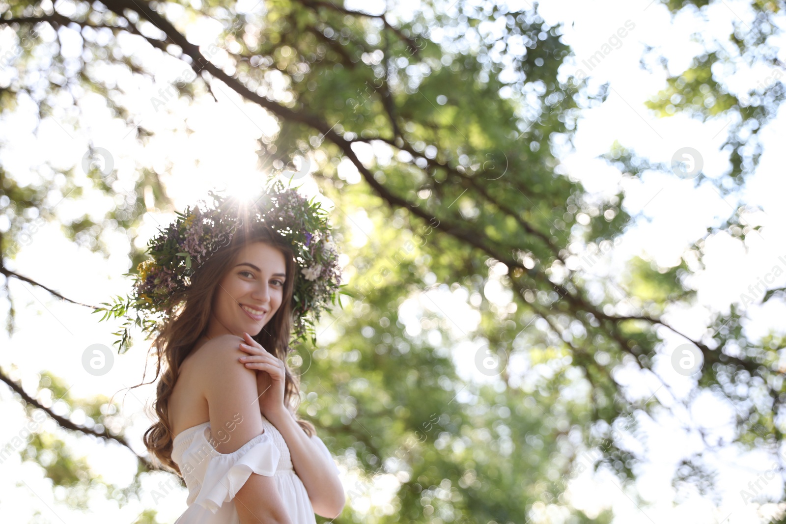 Photo of Young woman wearing wreath made of beautiful flowers outdoors on sunny day