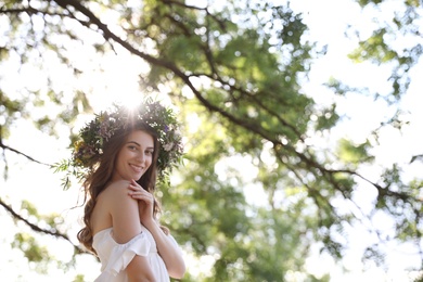 Young woman wearing wreath made of beautiful flowers outdoors on sunny day