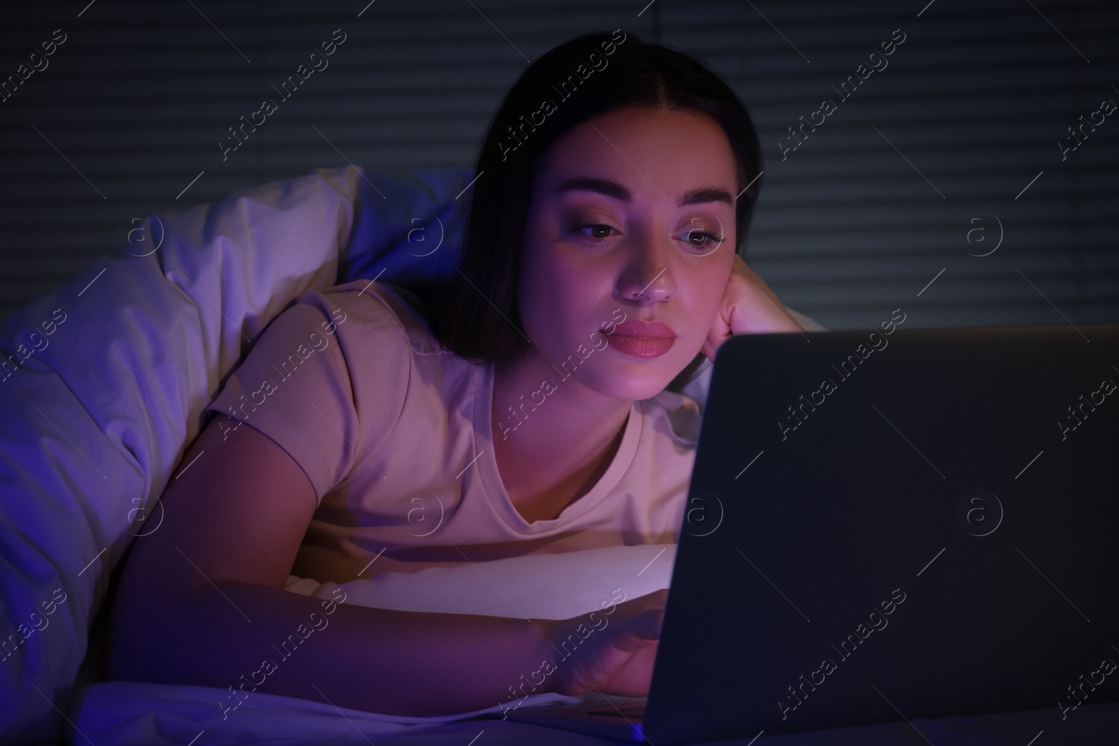 Photo of Young woman using laptop in bed at night. Internet addiction