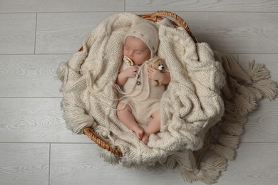 Photo of Adorable newborn baby with pacifier and toy bear sleeping in wicker basket on floor, top view