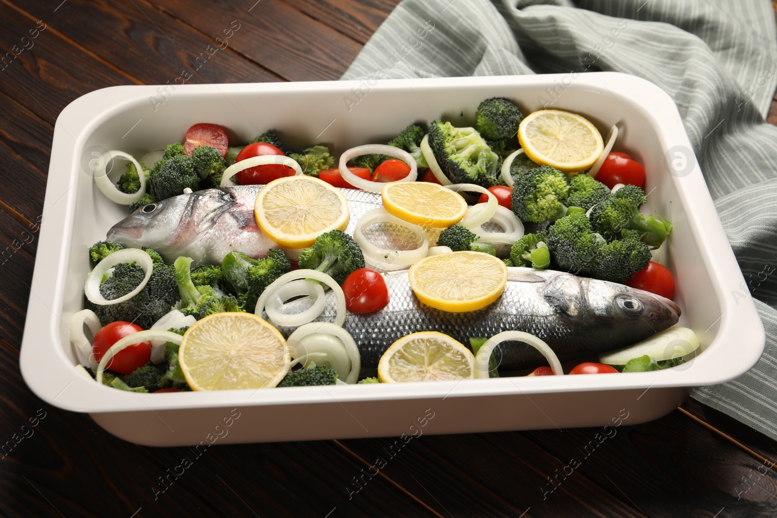 Photo of Raw fish with vegetables and lemon in baking dish on wooden table