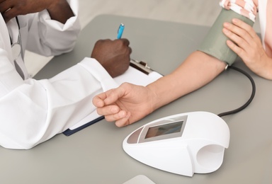 Photo of Young African-American doctor checking patient's blood pressure in hospital