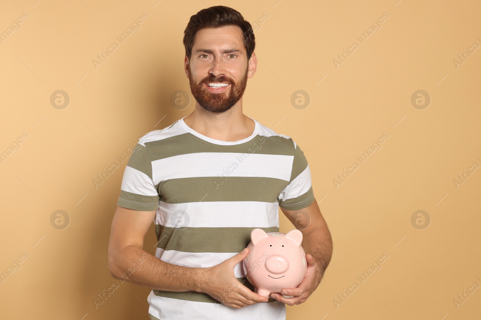 Photo of Happy man with ceramic piggy bank on beige background