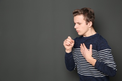 Photo of Teenage boy suffering from cough on dark background. Space for text