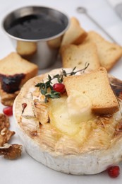 Photo of Tasty baked camembert with crouton, thyme, walnuts and pomegranate seeds on white table, closeup