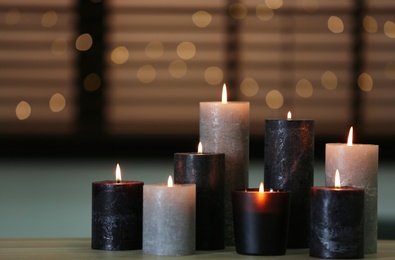 Photo of Beautiful burning candles on wooden table against festive lights. Space for text