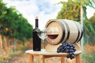 Photo of Bottle of wine, barrel and glasses on wooden table in vineyard