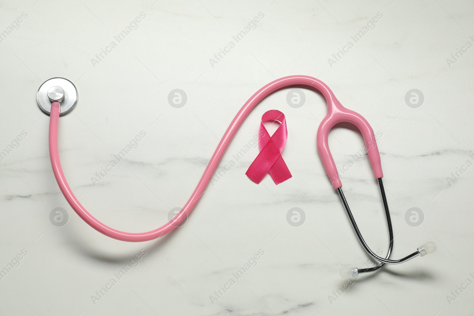 Photo of Pink ribbon and stethoscope on white marble table, flat lay. Breast cancer awareness