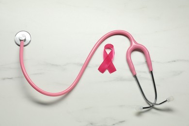 Photo of Pink ribbon and stethoscope on white marble table, flat lay. Breast cancer awareness