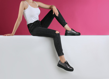 Woman in stylish shoes sitting on color background, closeup