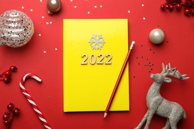 Photo of Yellow planner and Christmas decor on red background, flat lay. Planning for 2022 New Year