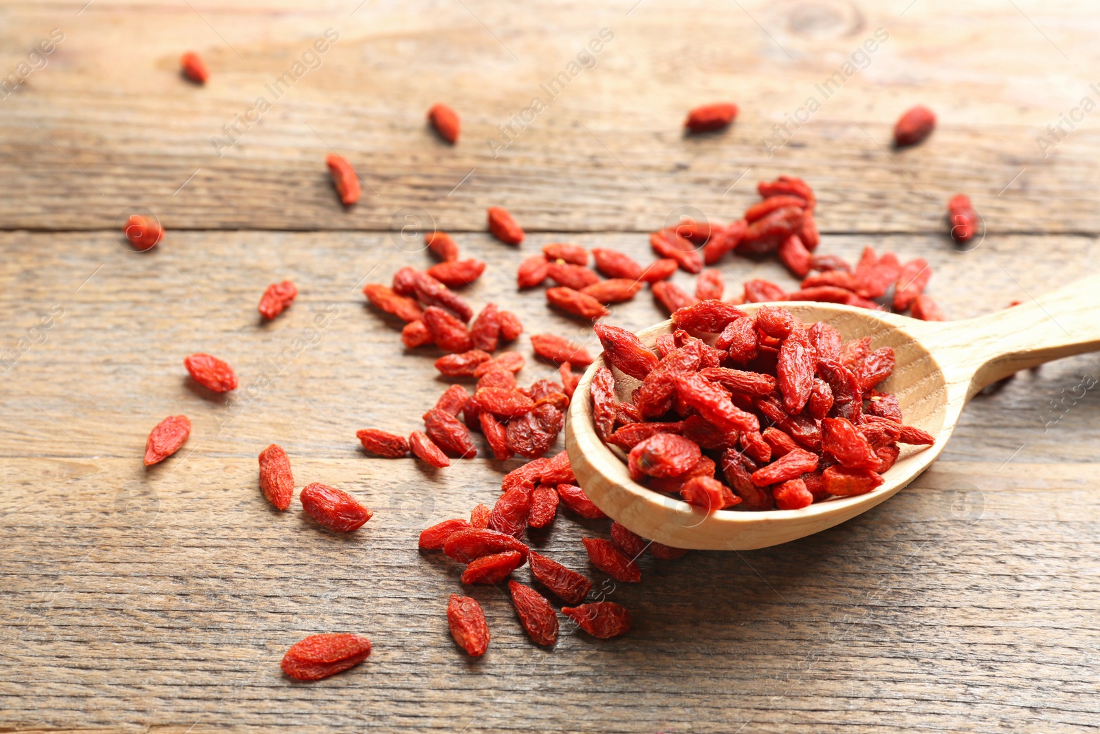 Photo of Spoon and dried goji berries on wooden table, closeup. Healthy superfood