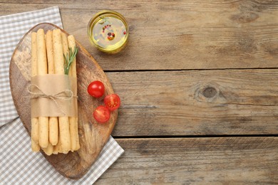 Photo of Tasty grissini with rosemary, oil and tomatoes on wooden table, flat lay. Space for text
