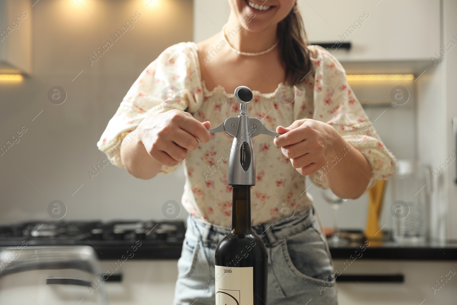 Photo of Smiling woman opening wine bottle with corkscrew in kitchen, closeup