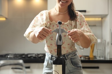 Photo of Smiling woman opening wine bottle with corkscrew in kitchen, closeup