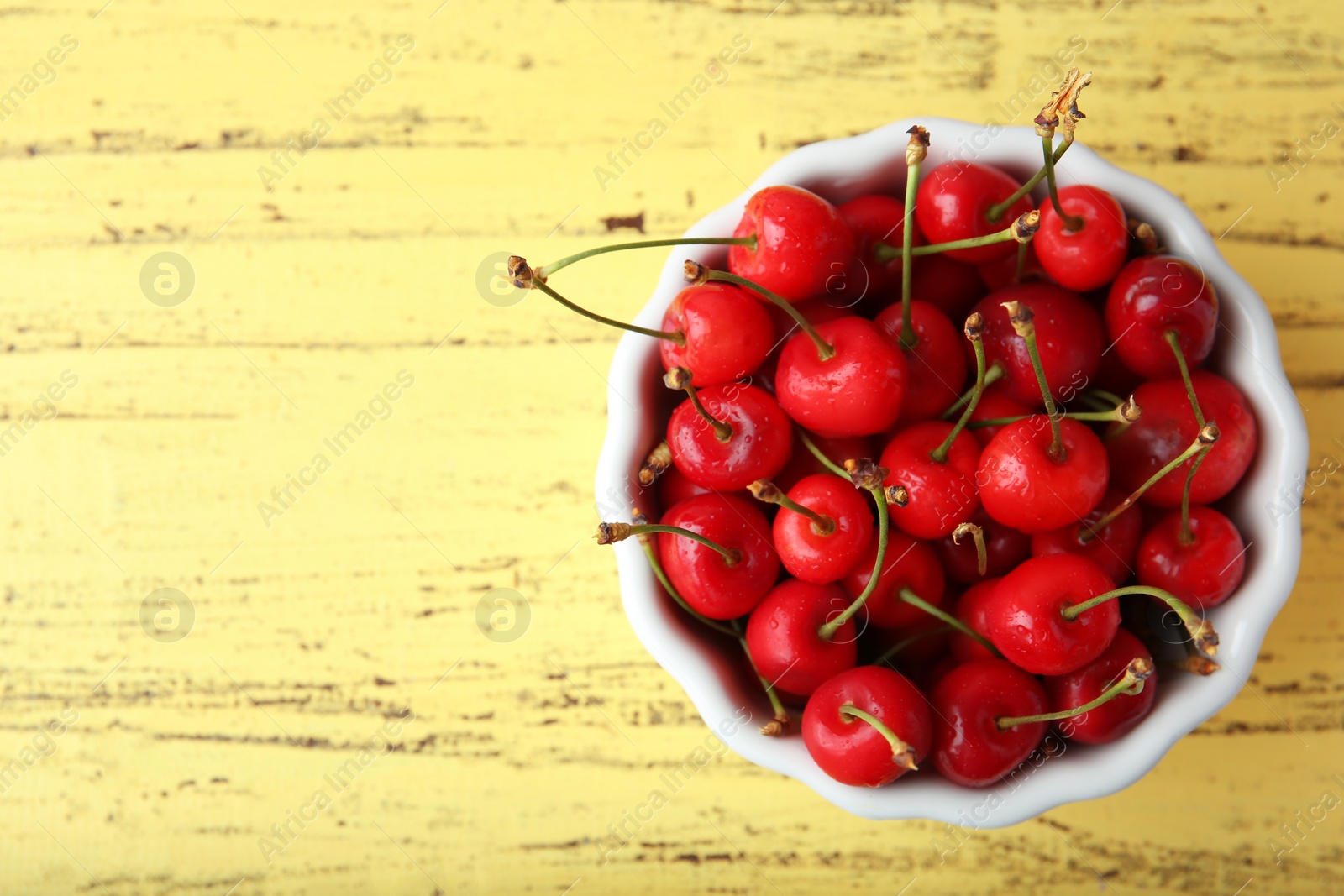 Photo of Bowl with ripe red cherries on wooden background, top view