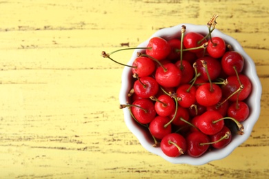 Bowl with ripe red cherries on wooden background, top view