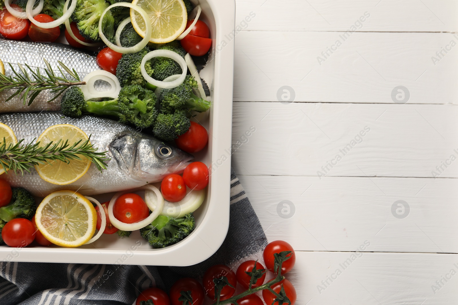 Photo of Raw fish with vegetables and lemon in baking dish on white wooden table, flat lay. Space for text