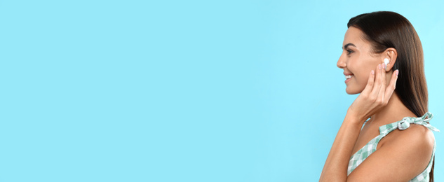 Image of Young woman listening to music with wireless earphones on turquoise background, space for text. Banner design