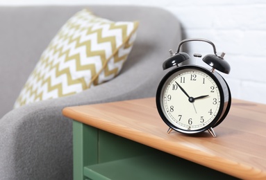 Analog alarm clock on side table in living room, space for text. Time of day