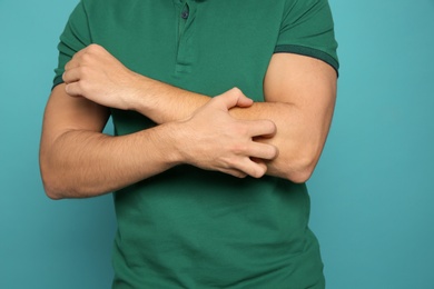 Photo of Young man scratching arm on color background, closeup. Annoying itch