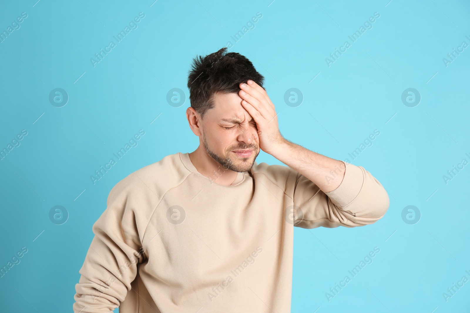 Photo of Man suffering from terrible migraine on light blue background