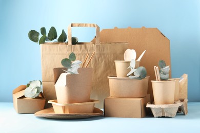 Photo of Eco friendly food packaging. Paper containers, tableware, bag and eucalyptus branches on white table against light blue background