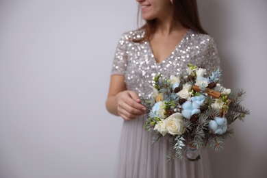 Bride holding beautiful winter wedding bouquet on light grey background, closeup. Space for text