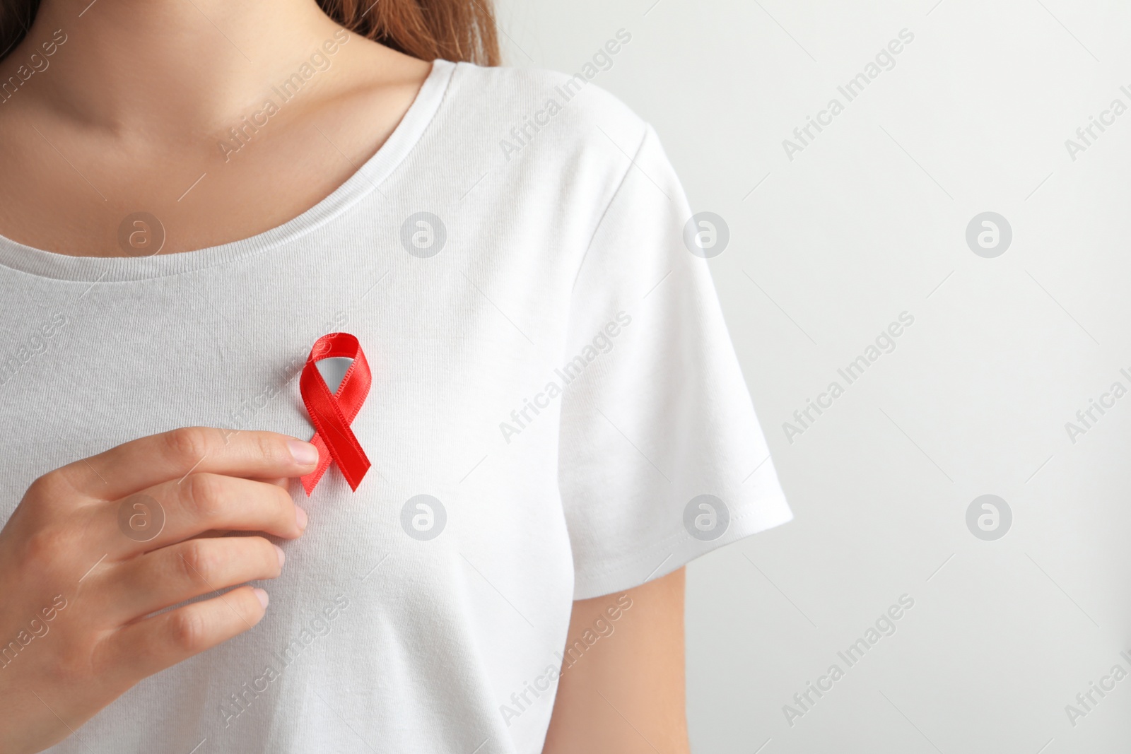 Photo of Woman with red ribbon on t-shirt against light background. Cancer awareness