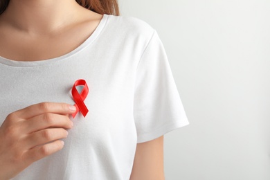 Woman with red ribbon on t-shirt against light background. Cancer awareness