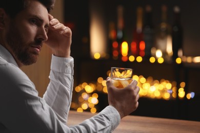 Man with glass of whiskey at bar counter against blurred lights. Space for text