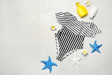 Photo of Flat lay composition with striped swimsuit and beach accessories on light stone background. Space for text